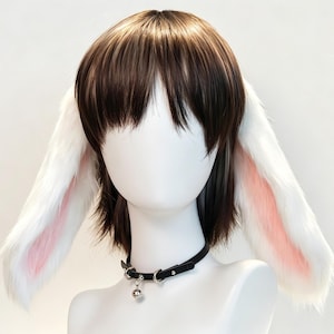 Puede incluir: Una peluca castaña con flequillo recto y capas largas, que presenta grandes orejas de conejo de felpa blanca con detalles interiores rosados a los lados. Un collar tipo gargantilla de cuero negro con herrajes plateados y una pequeña campana.
