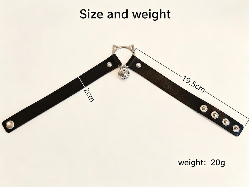 K&ouml;nnte beinhalten: Ein schwarzes Halsband aus leder&auml;hnlichem Material mit silberfarbenen Metallbeschl&auml;gen, einem katzenohrf&ouml;rmigen Ring und einer kleinen runden Glocke. Das Band ist 2cm breit und 19,5cm lang, bei einem Gewicht von 20g. Text Size and weight sichtbar.