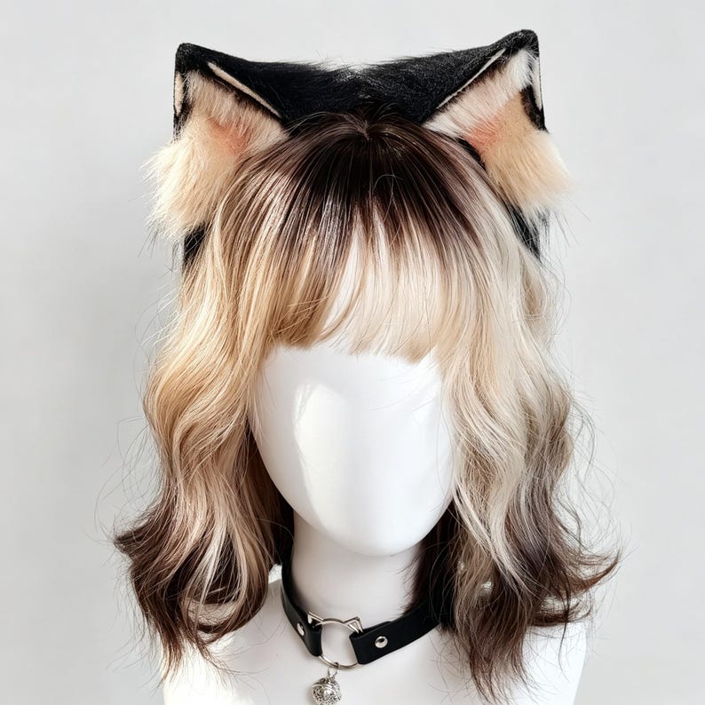 K&ouml;nnte beinhalten: Ein wei&szlig;er Schaufensterpuppenkopf mit einem schwarzen Halsband, das einen silbernen, katzenf&ouml;rmigen Ring und eine kleine Glocke aufweist. Die Puppe hat welliges, schulterlanges blondes Haar mit dunkelbraunem Ansatz und schwarze Kunstfell-Katzenohren.