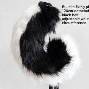K&ouml;nnte beinhalten: Ein Kunstfell-Schwanz-Accessoire mit schwarz-wei&szlig;em Muster. Es verf&uuml;gt &uuml;ber eine integrierte Befestigungsplatte und einen 120 cm langen, abnehmbaren schwarzen G&uuml;rtel mit verstellbarem Taillenumfang. Die langen Fasern sorgen f&uuml;r eine buschige Optik.