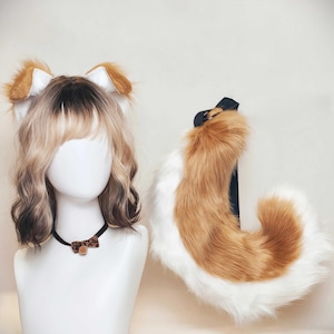 Op de afbeelding: Een set bruin-witte imitatiebont dierenoren, een bijpassende lange imitatiebont staart met een zwarte riem, en een zwarte choker met een kleine strik met luipaardprint, getoond op een etalagepophoofd met een blonde en bruine pruik.