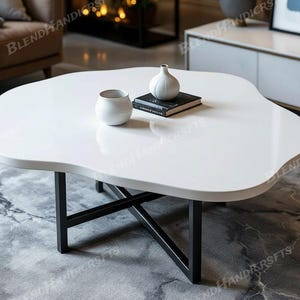 Puede incluir: Mesa de centro blanca de forma orgánica con patas de metal negro. La mesa tiene un acabado brillante y presenta dos jarrones de cerámica blancos y un libro encima. La mesa mide aproximadamente 100 cm de largo y 75 cm de ancho.
