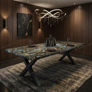 May include: A rectangular dining table featuring a polished blue and gold gemstone slab top with a natural veined pattern, supported by a black metal X-shaped base. The table is set with black plates, clear glasses, and dark grey vases.