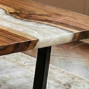 May include: Close-up of a wooden table with a white resin inlay. The table features a natural wood grain pattern with a glossy finish. The table has black metal legs and is a unique piece of furniture.