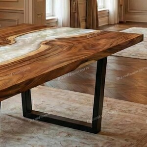 May include: A handcrafted wooden table with a live edge design. The table features a river of white resin flowing through the center, framed by rich brown wood. It is supported by black metal legs, creating a modern and natural aesthetic.
