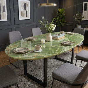Può includere: Un tavolo da pranzo ovale con piano in pietra onice verde lucida e struttura in metallo nero, circondato da sei sedie imbottite grigie. Il tavolo è apparecchiato con piatti in ceramica bianca, posate, un vaso bianco con verde e una candela.