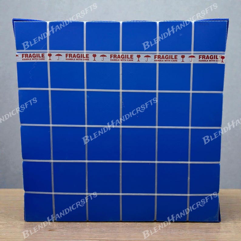 May include: A blue box with a grid pattern and white lines. The box is sealed with tape that reads "FRAGILE HANDLE WITH CARE" with a graphic of a wine glass. The box has the words "BLEND HANDICRSFTS" printed on it.