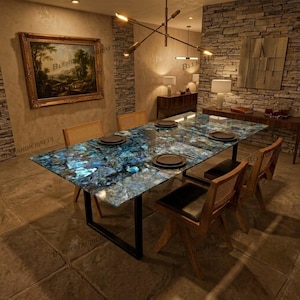 Puede incluir: Una mesa de comedor rectangular con una superficie de ágata azul pulida con un patrón cristalino natural, sostenida por un marco de metal negro. La mesa está puesta con platos oscuros y rodeada por cuatro sillas de madera clara.