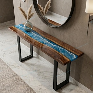 May include: A wooden console table with a blue resin river design. The table has a dark wood finish and black metal legs. A clear glass vase with dried plants sits on top.