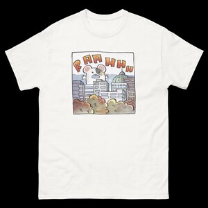 May include: White t-shirt featuring a cartoon illustration of a mouse in a city. The mouse is depicted with its arms raised, with the word "RAHHH" above it. The background includes buildings, trees, and a dome-shaped structure.