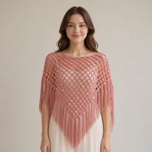 May include: A dusty rose crochet poncho featuring an open diamond-shaped lattice pattern with small integrated sequins. The garment has a wide neckline and long, straight fringe trim along the bottom edges, creating a pointed triangular silhouette.