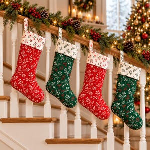 Può includere: Quattro calze di Natale appese a una ringhiera di una scala in legno bianco. Due calze sono rosse e due sono verdi, tutte con un motivo botanico bianco di rametti e bacche. Ogni calza ha un risvolto bianco con una stampa di bacche rosse.
