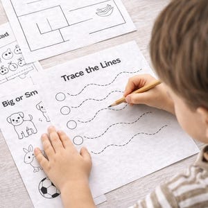 Puede incluir: Un niño traza líneas con un lápiz en una hoja de trabajo. La hoja de trabajo tiene el texto "Trace the Lines" e incluye líneas punteadas para practicar. También se ven otras hojas de trabajo con laberintos e ilustraciones.