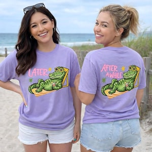 Peut inclure: Deux t-shirts lavande avec un motif de crocodile de dessin animé. L'un dit "LATER" et l'autre "AFTER AWHILE". Le crocodile porte des lunettes de soleil et se détend dans une chaise longue, tenant une boisson.