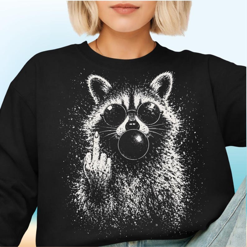 Pu&ograve; includere: Felpa nera con grafica bianca di un procione con occhiali da sole che fa una bolla. Il procione fa il dito medio. Il design ha un effetto vernice schizzata.