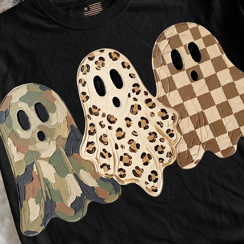 May include: A black t-shirt featuring three ghost figures with textured, raised paint-like details. The left ghost has a camouflage pattern, the center ghost has a leopard print, and the right ghost has a brown and beige checkered pattern.