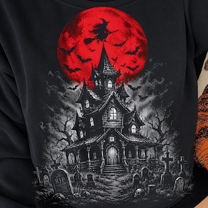May include: A black sweatshirt featuring a graphic print of a haunted house in a graveyard under a large red moon. The design includes a silhouette of a witch flying on a broomstick, numerous bats, bare trees, and tombstones with the text RIP.