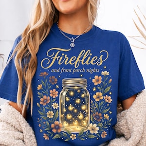 Pu&ograve; includere: T-shirt blu reale con la scritta dorata "Fireflies and front porch nights". Un barattolo pieno di lucciole luminose &egrave; circondato da fiori arancioni e gialli.