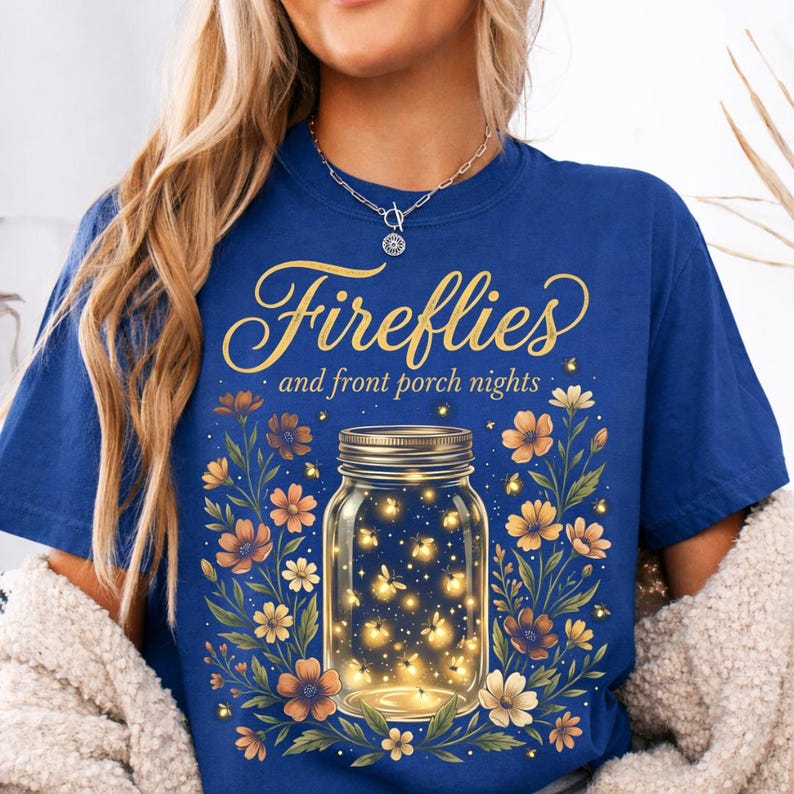 Pu&ograve; includere: T-shirt blu reale con la scritta dorata "Fireflies and front porch nights". Un barattolo pieno di lucciole luminose &egrave; circondato da fiori arancioni e gialli.