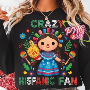 May include: Black sweatshirt with a colorful graphic of a doll wearing a traditional dress and holding a foam finger. The text reads "CRAZY HISPANIC FAN" in vibrant colors. Maracas and floral accents complete the design.