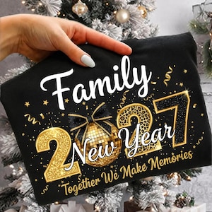 May include: A black t-shirt featuring the white text Family, the gold glitter numbers 2027, a gold disco ball with a black bow, and the text New Year Together We Make Memories in white and gold script, accented with gold confetti and stars.