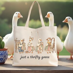 Może przedstawiać: Kremowa torba typu tote z fantazyjną ilustracją gęsi ubranych w odzież w stylu vintage. Poniżej ilustracji znajduje się napis "just a thrifty goose". Torba ma jasny uchwyt i jest otoczona białymi gęsiami.