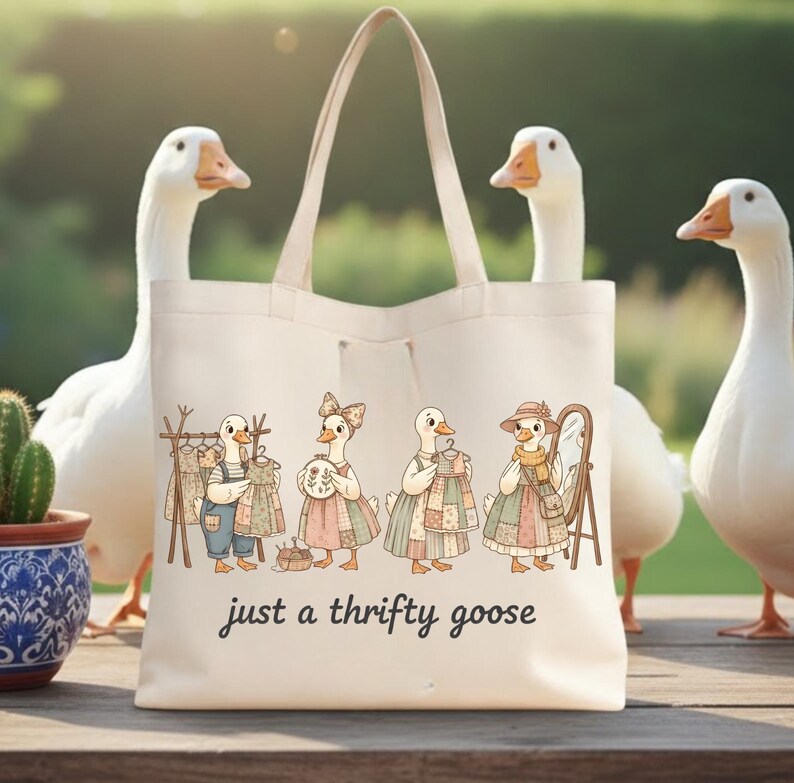 Może przedstawiać: Kremowa torba typu tote z fantazyjną ilustracją gęsi ubranych w odzież w stylu vintage. Poniżej ilustracji znajduje się napis "just a thrifty goose". Torba ma jasny uchwyt i jest otoczona białymi gęsiami.