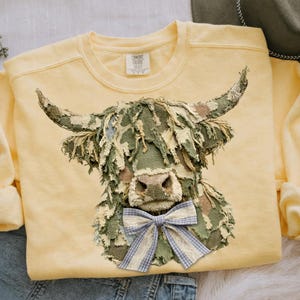 May include: A white ceramic mug with a black handle and the text "But First, Coffee" in a bold, black font. The mug is set against a blurred background, suggesting a cosy setting.