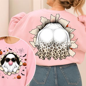 May include: A light pink sweatshirt featuring a graphic on the back of a white ghost with a leopard print bottom edge emerging from a torn paper effect. The front graphic shows a white ghost wearing leopard print sunglasses and blowing a pink bubble.