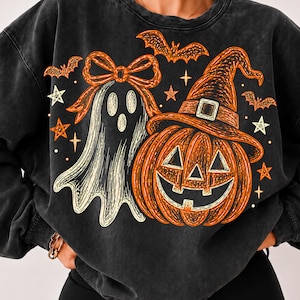 May include: A charcoal gray crewneck sweatshirt featuring a graphic print of a white ghost with an orange bow, an orange jack-o'-lantern wearing a witch hat, and several orange and white bats and stars scattered across the front of the garment.