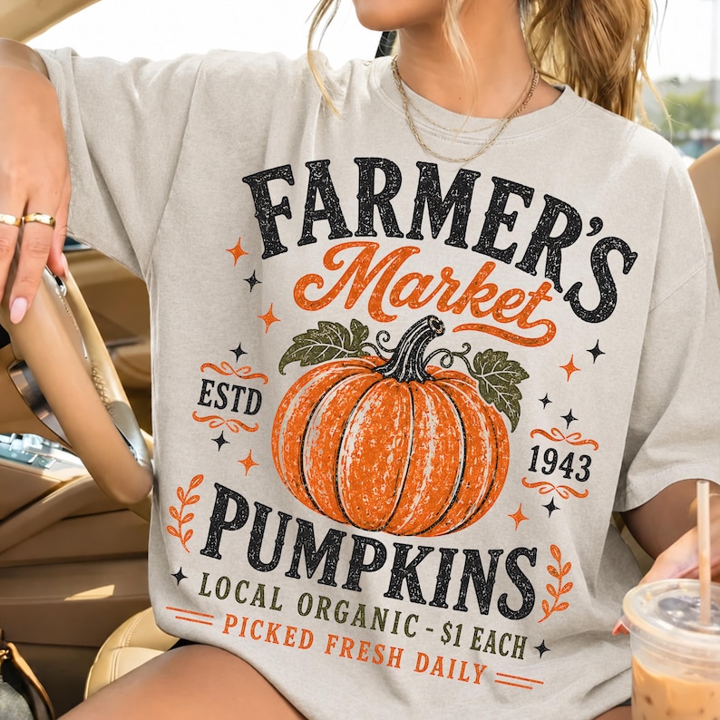 Puede incluir: Una camiseta de color beige claro con un estampado gr&aacute;fico que incluye el texto FARMER'S MARKET PUMPKINS, ESTD 1943, LOCAL ORGANIC - $1 EACH y PICKED FRESH DAILY. El dise&ntilde;o muestra una calabaza naranja grande con hojas verdes y estrellas.