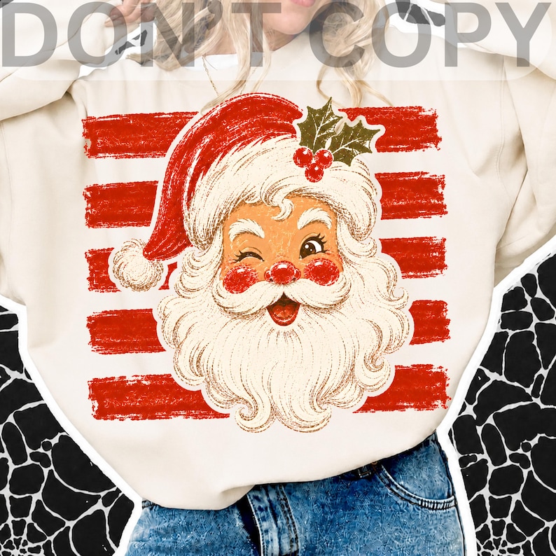 May include: A cream-colored sweatshirt featuring a graphic of a winking Santa Claus with a red hat, rosy cheeks, and a white beard. The design includes a sprig of green holly with red berries above Santa and horizontal red brushstroke stripes.