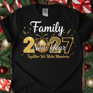 May include: A black short-sleeve t-shirt featuring a gold and black graphic with the text Family New Year 2027 Together We Make Memories. The design includes a gold glittery number 2, a disco ball with a black bow, and a leopard print number 27.