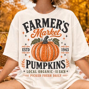 Puede incluir: Una camiseta de manga corta color hueso con un gr&aacute;fico de una calabaza naranja con hojas verdes. El texto dice: FARMER'S MARKET, ESTD 1943, PUMPKINS, LOCAL ORGANIC - $1 EACH, PICKED FRESH DAILY, rodeado de peque&ntilde;as estrellas y hojas.