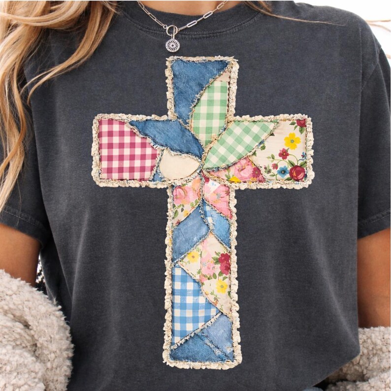 May include: Dark grey t-shirt with a patchwork cross design. The cross is made from denim, gingham, and floral fabrics, with a cream border. The shirt has short sleeves and a crew neck. The measurements are in centimetres.