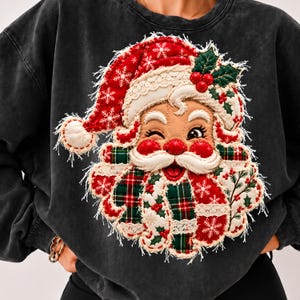 Può includere: Una felpa girocollo grigio antracite con una grande applicazione tridimensionale del volto di Babbo Natale che fa l'occhiolino. Il design è realizzato in tessuto trapuntato a quadri rossi e verdi, pizzo bianco e fiocchi di neve ricamati.