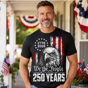 May include: Black t-shirt featuring a patriotic design with an American flag motif. The shirt includes an eagle illustration, the text "We the People," and the years "1776" and "2026," celebrating 250 years.