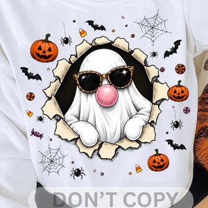 May include: A white t-shirt featuring a graphic of a white ghost wearing leopard print sunglasses and blowing a pink bubble. The ghost is emerging from a torn paper effect surrounded by orange jack-o'-lanterns, black bats, spiders, webs, and candy.