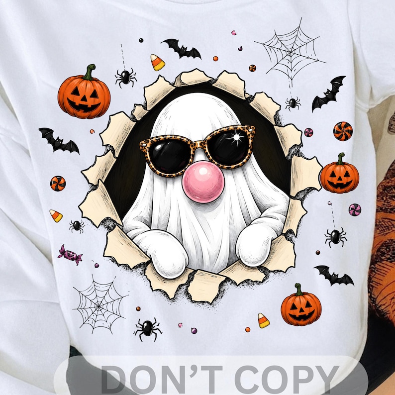 May include: A white t-shirt featuring a graphic of a white ghost wearing leopard print sunglasses and blowing a pink bubble. The ghost is emerging from a torn paper effect surrounded by orange jack-o'-lanterns, black bats, spiders, webs, and candy.