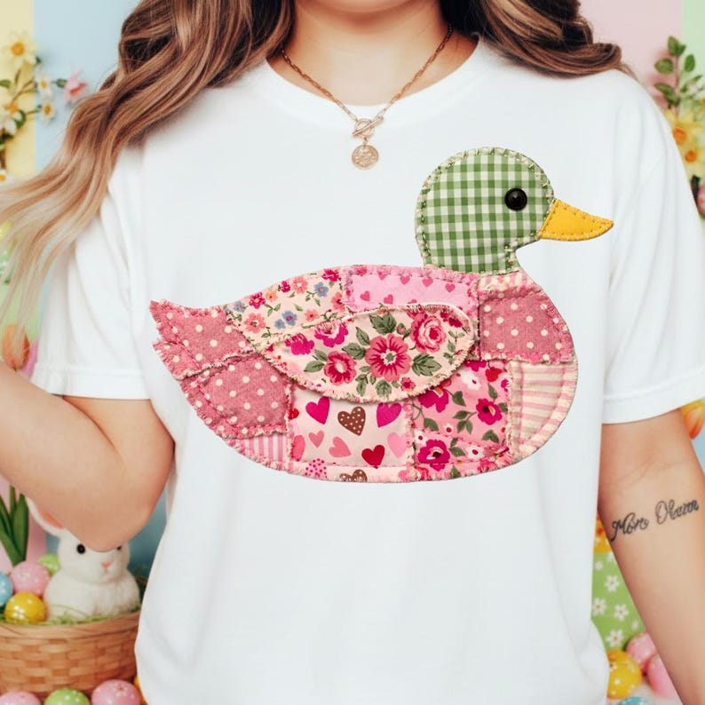 K&ouml;nnte beinhalten: Wei&szlig;es T-Shirt mit einem Patchwork-Enten-Design. Die Ente hat einen gr&uuml;nen Vichy-Kopf, einen gelben Schnabel und einen K&ouml;rper aus rosa Blumen- und Polka-Dot-Stoffen. Das Design ist mittig auf dem Shirt platziert.