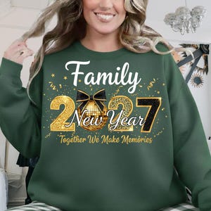 May include: A dark green long-sleeve sweatshirt featuring the text Family New Year and Together We Make Memories in white and gold. The design includes a gold disco ball with a black bow, gold confetti, and the year 2027 in gold and black.