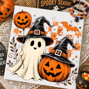 Può includere: Una stampa su tela quadrata raffigurante un fantasma bianco con un cappello da strega nero che tiene un palloncino a forma di zucca arancione, accanto a una grande zucca arancione con un cappello da strega nero, su uno sfondo a scacchi arancione.