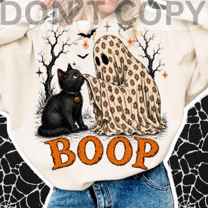 May include: A cream-colored sweatshirt featuring a graphic of a black cat wearing a purple collar with a pumpkin charm, being touched on the nose by a ghost covered in a tan floral sheet. The design includes bare trees, bats, and the word BOOP.