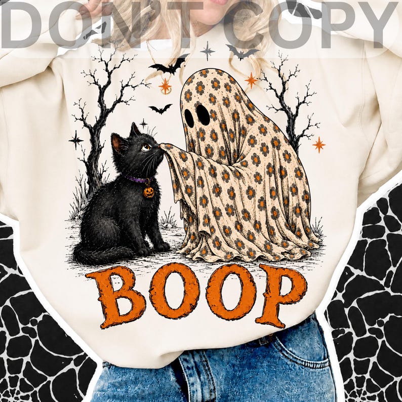 May include: A cream-colored sweatshirt featuring a graphic of a black cat wearing a purple collar with a pumpkin charm, being touched on the nose by a ghost covered in a tan floral sheet. The design includes bare trees, bats, and the word BOOP.