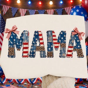 Könnte beinhalten: Ein cremefarbenes Sweatshirt mit dem Wort "MAMA" in Patchwork-Optik. Die Buchstaben zeigen eine Kombination aus amerikanischen Flaggenmustern, Denim und Leopardenmuster. Rot-weiß gestreifte Schleifen akzentuieren die oberen Ecken.