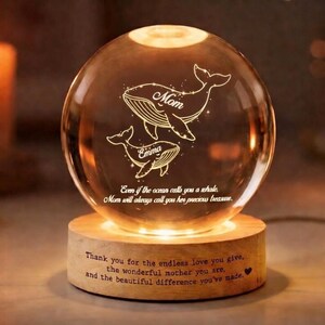 Könnte beinhalten: Eine leuchtende Kristallkugel mit Waldesign, die auf einem Holzsockel steht. Die Kugel ist mit den Worten "Mom" und "Emma" sowie einer herzlichen Botschaft graviert. Der Sockel strahlt ein warmes Licht aus.