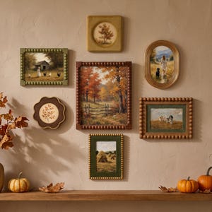 May include: A gallery wall arrangement featuring six framed landscape paintings with various textures and shapes, including beaded, oval, and scalloped frames, displaying scenes of rural life, autumn trees, haystacks, and animals on a beige wall.