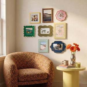 May include: A gallery wall arrangement featuring eight diverse picture frames in various shapes and colours, including yellow, green, blue, pink, and wood tones, surrounding a leopard print armchair and a yellow side table with orange flowers.