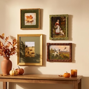 Peut inclure: Un ensemble de cadres muraux comprenant trois cadres rectangulaires à bords perlés et un cadre doré avec un passe-partout vert. Les images représentent une feuille d'érable, une personne avec un chien et une scène de chasse. Vase et citrouilles.