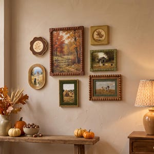 May include: A gallery wall arrangement featuring six framed landscape paintings with various shapes and textures, including beaded and scalloped edges. The artwork depicts autumn scenes, rural farm life, and fields, displayed above a wooden console table.